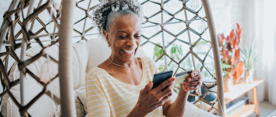 a mature woman holding a credit/debit card preparing to make a mobile purchase